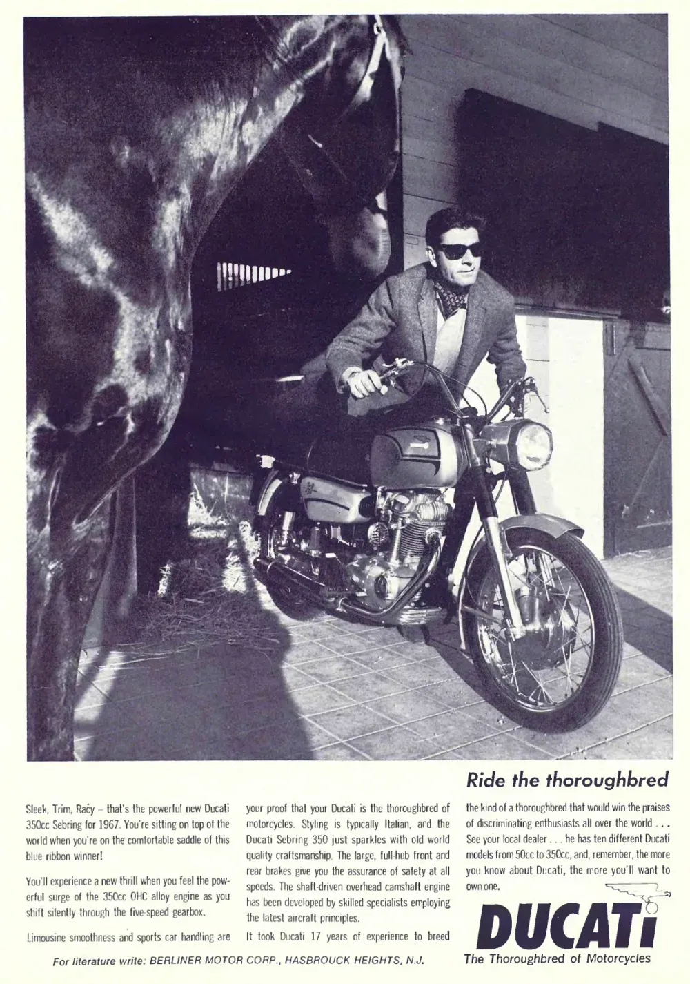 Rider in sunglasses straddles a Ducati Sebring motorcycle beside a dark horse in a stable.