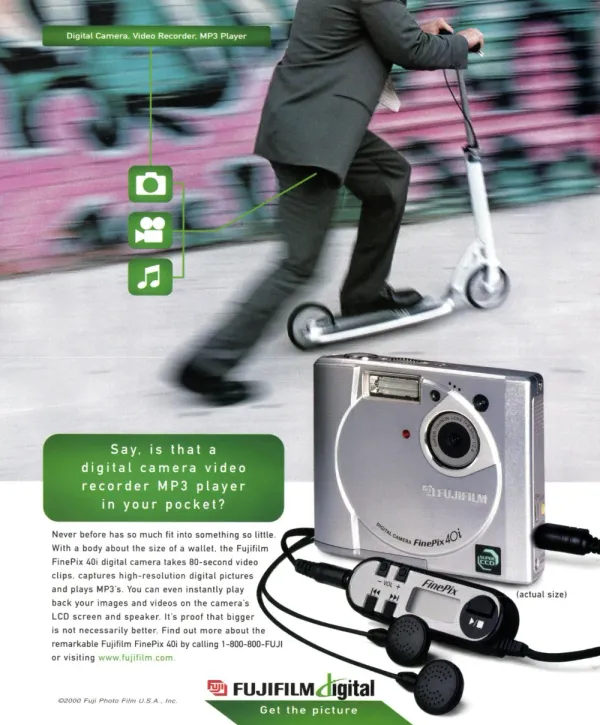 A suited man rides a kick scooter past a blurred wall while a Fujifilm FinePix 40i camera and its wired music remote fill the foreground.