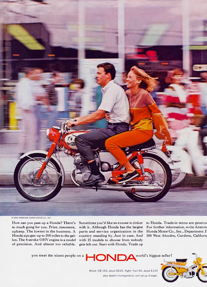 A smiling passenger rides behind a man on a red Honda CB 160 past blurred shopfronts, with a small yellow Trail 90 below.