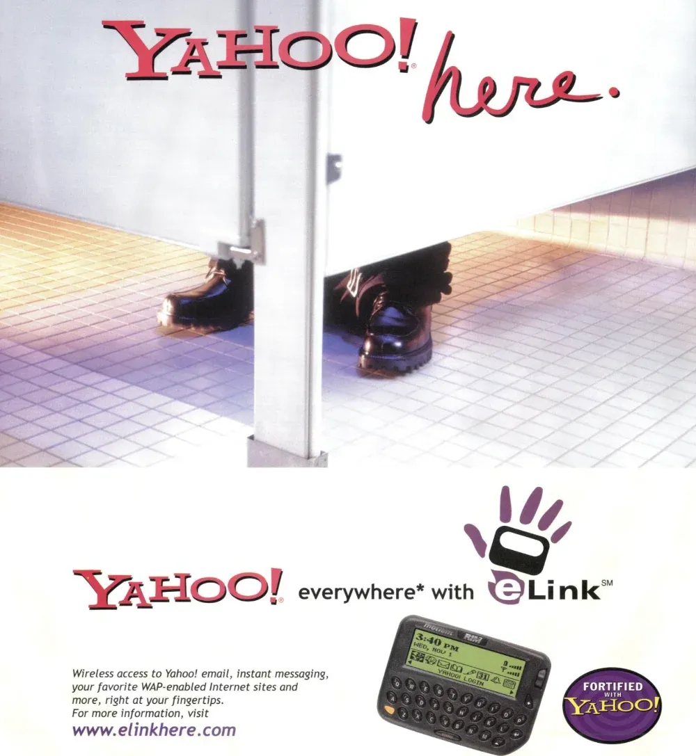 Yahoo! here headline above shoes visible beneath a restroom stall, with an eLink handheld, wireless-access copy, and a Fortified with Yahoo! badge below.